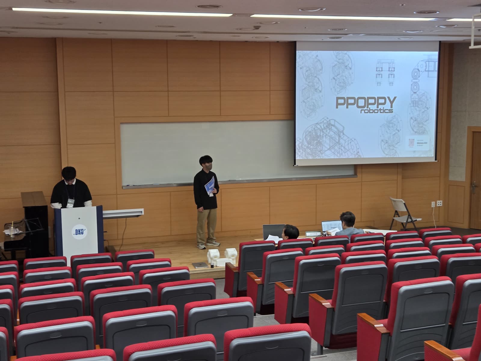 강의실 무대에서 PPOPPY robotics 슬라이드를 띄우고 발표하는 팀.